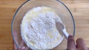 Mixing cake batter in a glass bowl with a spatula on a wooden countertop.